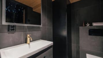 Een moderne badkamer met een witte wasbak, een gouden kraan en donkere tegels.