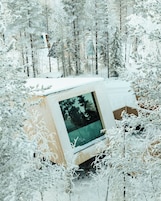 A snow-covered cabin with a large window, surrounded by trees.
