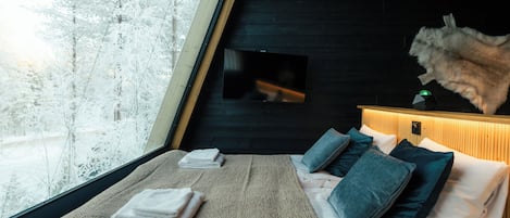 A cozy room with a bed, a window with a view of snow-covered trees, and a fireplace.