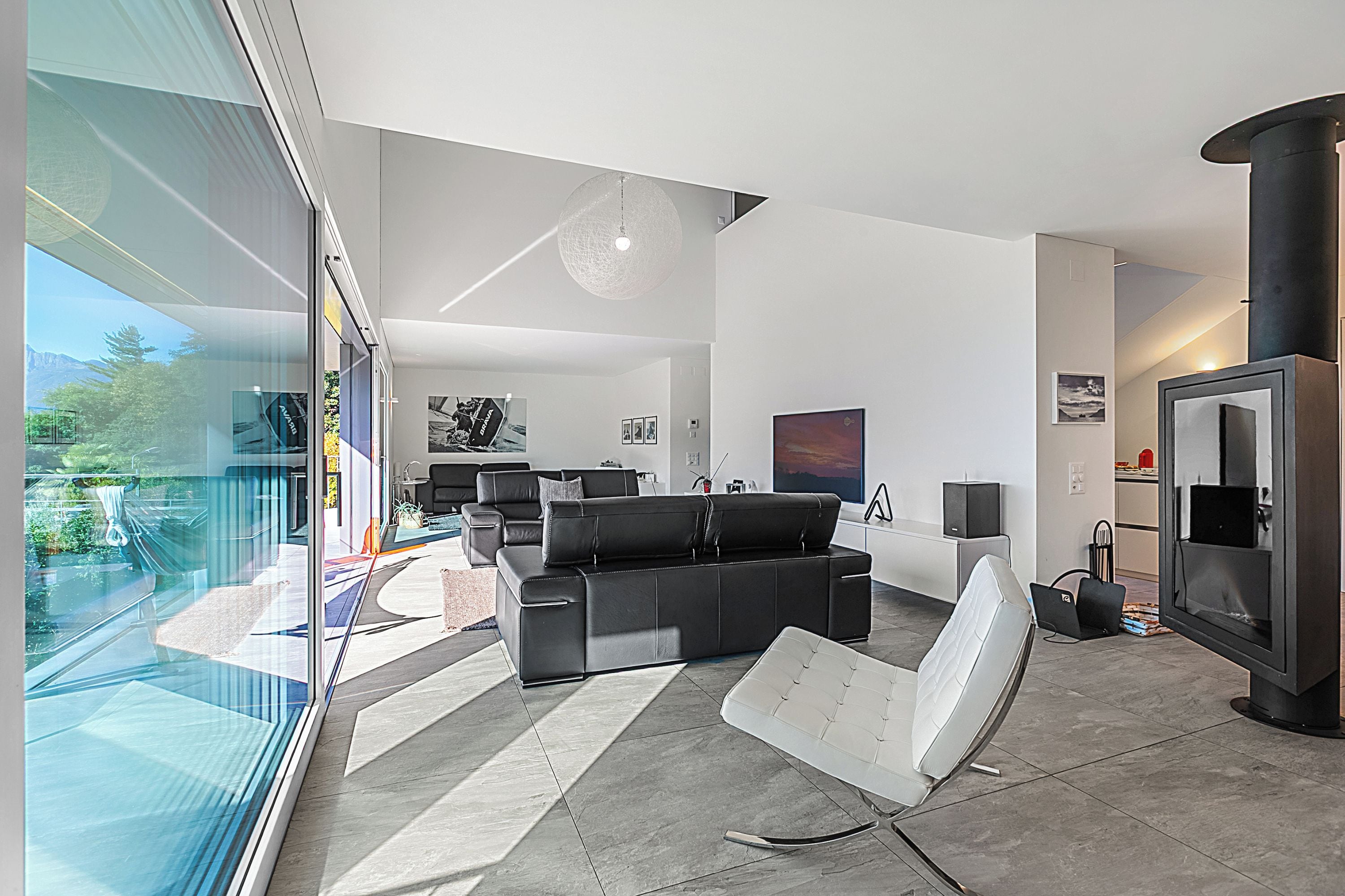 A modern living room with a black leather sofa, a white chair, and a fireplace.