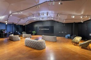 A spacious room with a wooden floor, a large screen displaying 'W AMSTERDAM,' and several seating areas. - W Amsterdam (Amsterdam)