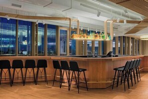 A bar area with a long counter, multiple bar stools, and a view of the city through large windows. - W Amsterdam (Amsterdam)