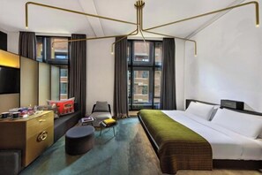 Une chambre d’hôtel moderne, dotée d’un grand lit, d’un bureau avec une chaise, d’un canapé et d’une grande fenêtre avec des rideaux.