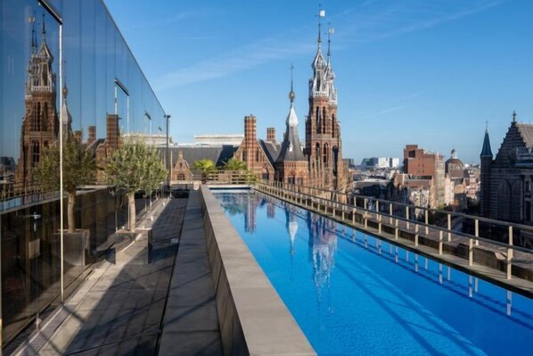 Une piscine sur le toit offrant une vue panoramique sur la ville, avec ses bâtiments historiques et un ciel dégagé.