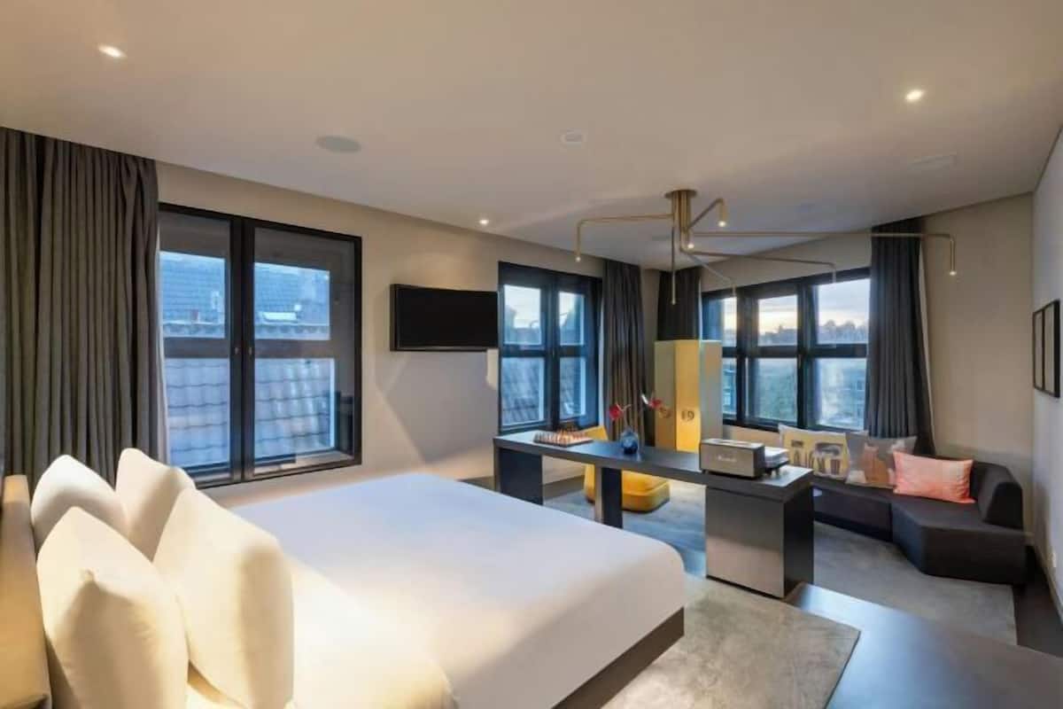 A modern hotel room with a large bed, a desk, a sofa, and a TV.