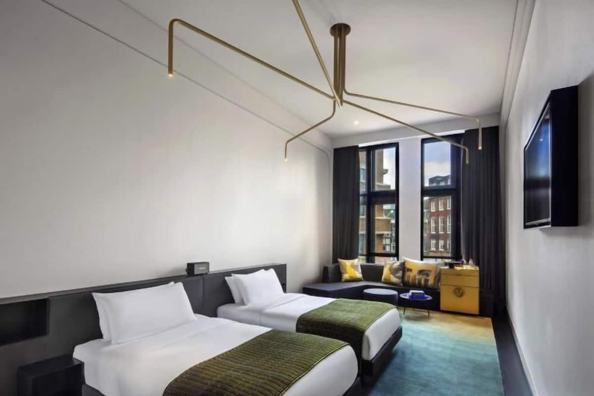 A hotel room with two beds, a sofa, a TV, and a view of buildings.