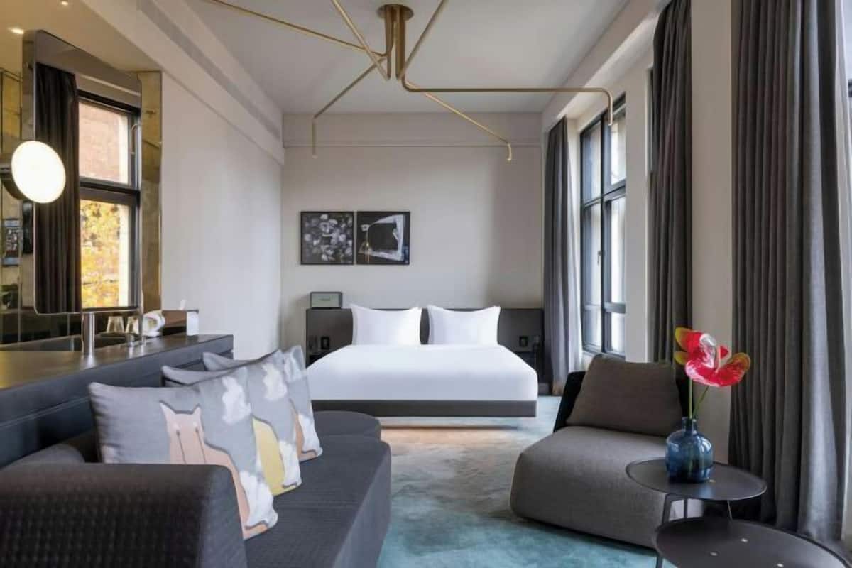 A modern hotel room with a large bed, a sofa, a small table, and a mirror.