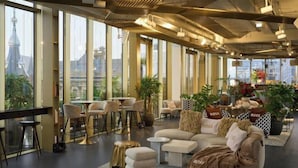 A modern lounge area with large windows, comfortable seating, and a variety of plants. - W Amsterdam (Amsterdam)