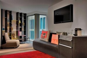 A modern living room with a sofa, a TV mounted on the wall, and a bookshelf filled with books and decorative items.