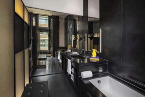 Een moderne badkamer met een donker kleurenschema, een grote spiegel en een bad.