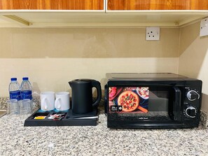 A kitchen with a microwave and a kettle on the counter, a tray with cups and bottles, and a power outlet on the wall.