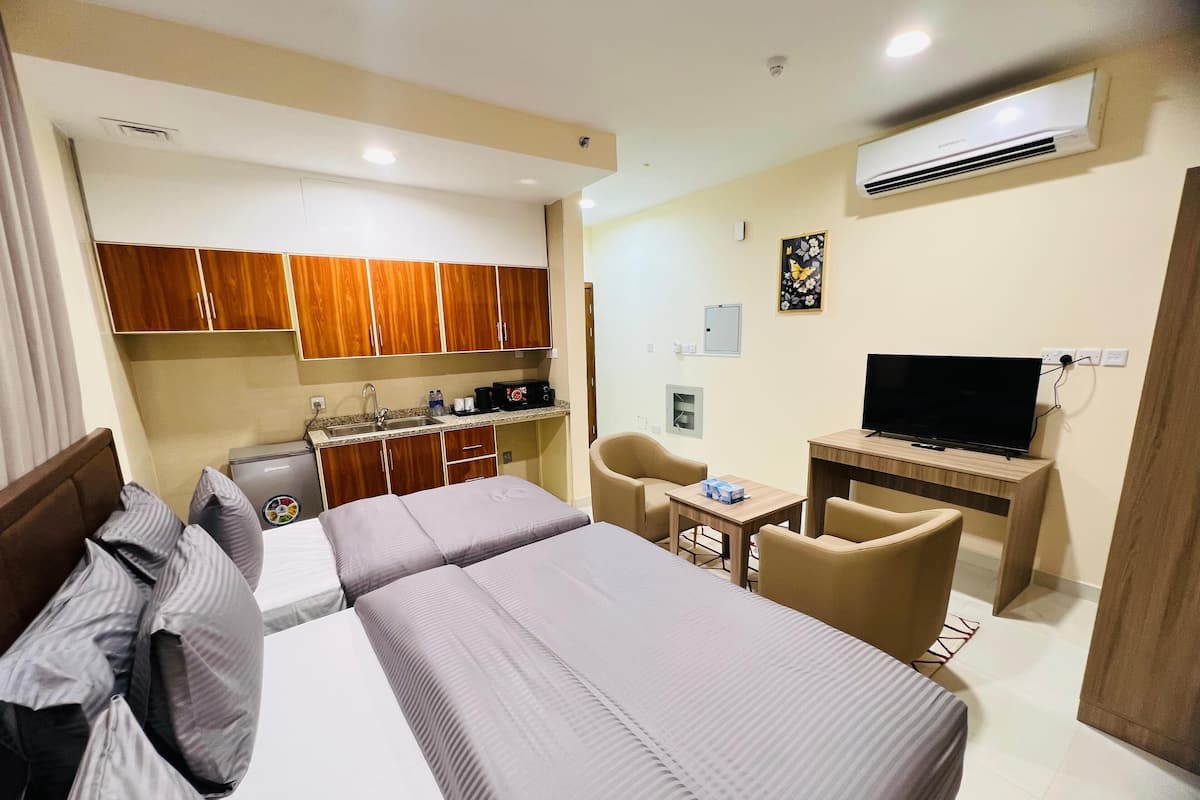 A hotel room with a kitchenette, a TV, a desk, and two beds.