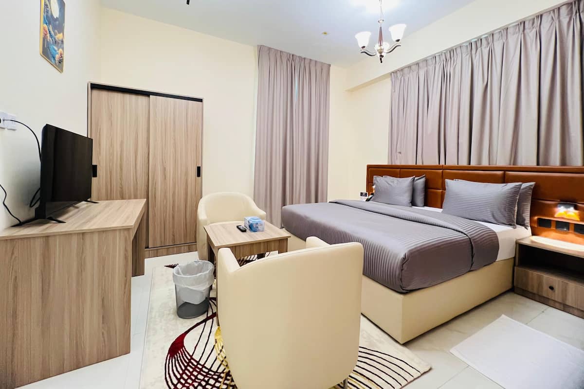 A hotel room with a bed, a desk with a TV, a chair, and a small table.