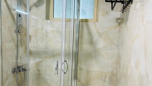 Cabina de ducha con paredes de vidrio, un cabezal de ducha de mano y un perchero con toallas dobladas.
