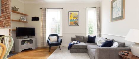 Un salon avec un canapé gris, un téléviseur, un fauteuil et une lampe.