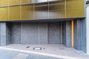 Entrada de un edificio con barandilla metálica, pared de concreto y una puerta con un logotipo.