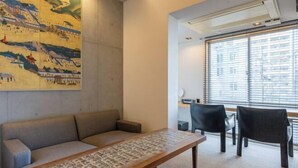 Une chambre moderne avec un canapé, une table en bois et une grande fenêtre équipée de stores.
