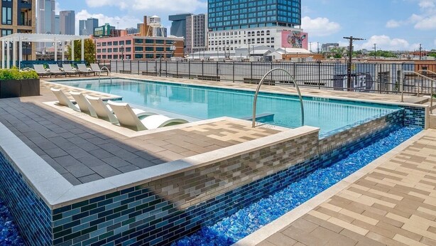 Ein Pool auf dem Dach mit Blick auf die Stadt, umgeben von Gebäuden und blauem Himmel.