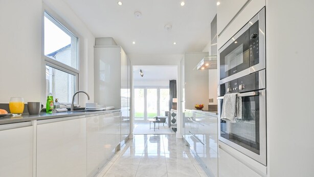 A modern kitchen with white cabinetry, a stainless steel oven, and a large window providing natural light. - The Grove by Tŷ SA (Cardiff)