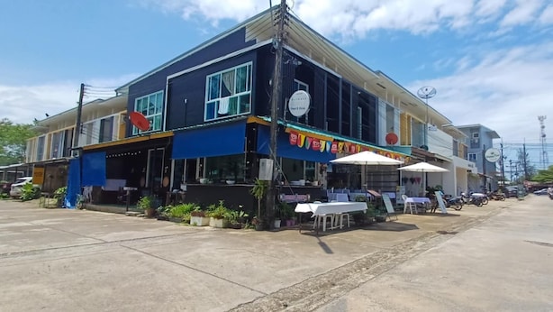 A two-story building with a blue facade, outdoor seating, and a sign indicating food and drink services. - Burmese Corner (Khao Lak)