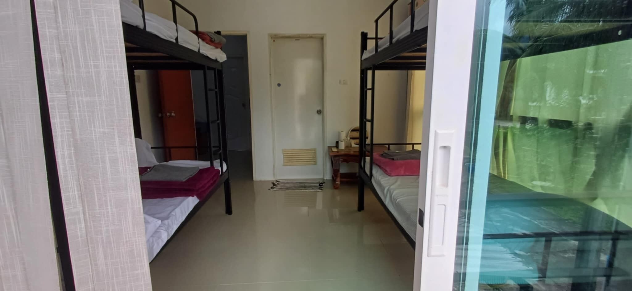 A corridor with bunk beds, a door, a small table with a lamp, and a window with a view.