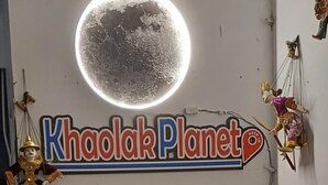 A reception desk with a computer monitor, a sign reading 'Khaolak Planet,' and a decorative moon on the wall. - Burmese Corner (Khao Lak)