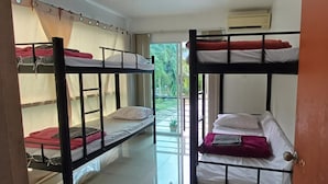 A dormitory room with bunk beds, a sliding door, and a view of greenery outside. - Burmese Corner (Khao Lak)