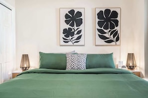 Un lit avec une literie verte, deux tableaux floraux encadrés accrochés au mur et deux lampes de chevet.