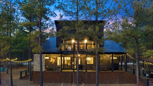 A two-story lodge with a stone foundation, wooden deck, and a covered outdoor area.