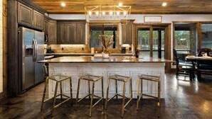 A modern kitchen with a central island, bar stools, and a stainless steel refrigerator.