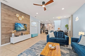 A modern living room with a wooden accent wall, a ceiling fan, a flat-screen TV, a blue sofa, and a wooden coffee table.
