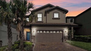 A two-story house with a garage, a blue door, and a brick driveway. - Magic Moments Villa  • Private Pool • Games (Kissimmee)
