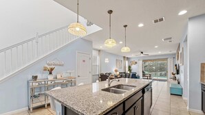 A spacious kitchen with granite countertops, a central island with a sink, and pendant lighting. - Magic Moments Villa  • Private Pool • Games (Kissimmee)