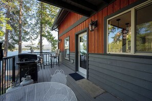 Terraza de madera con una parrilla y mobiliario exterior, con vista a un cuerpo de agua.