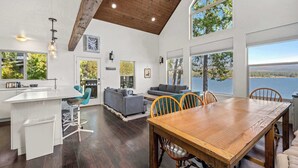 A spacious living area with a wooden dining table, a gray sofa, and a kitchen island with bar stools. - Lakefront Hayden Lake Home with Private Dock for Family Getaways (Hayden)