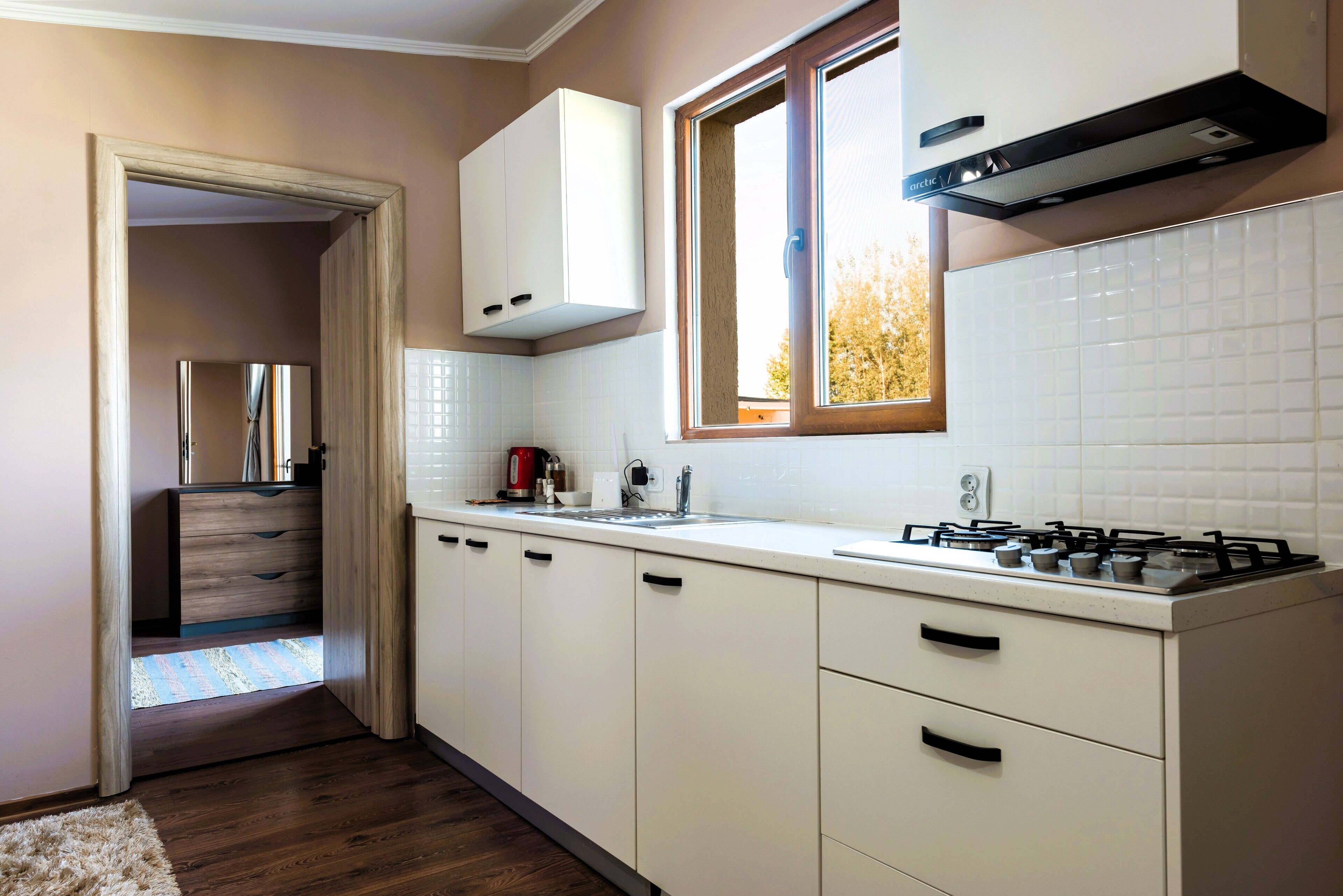A modern kitchen with white cabinets, a gas stove, and a window providing natural light.