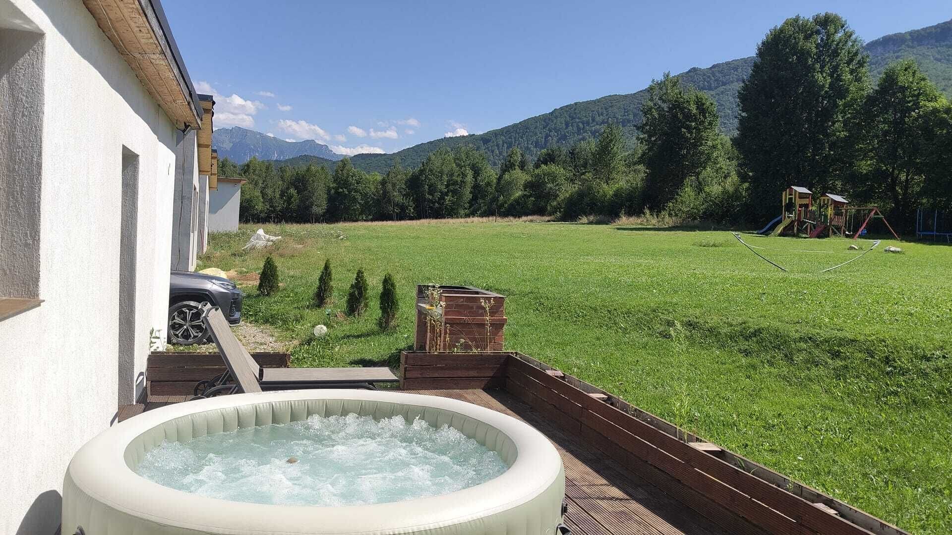 Ein Whirlpool auf einer Holzterrasse mit einem Rasen und einer Bergkulisse.