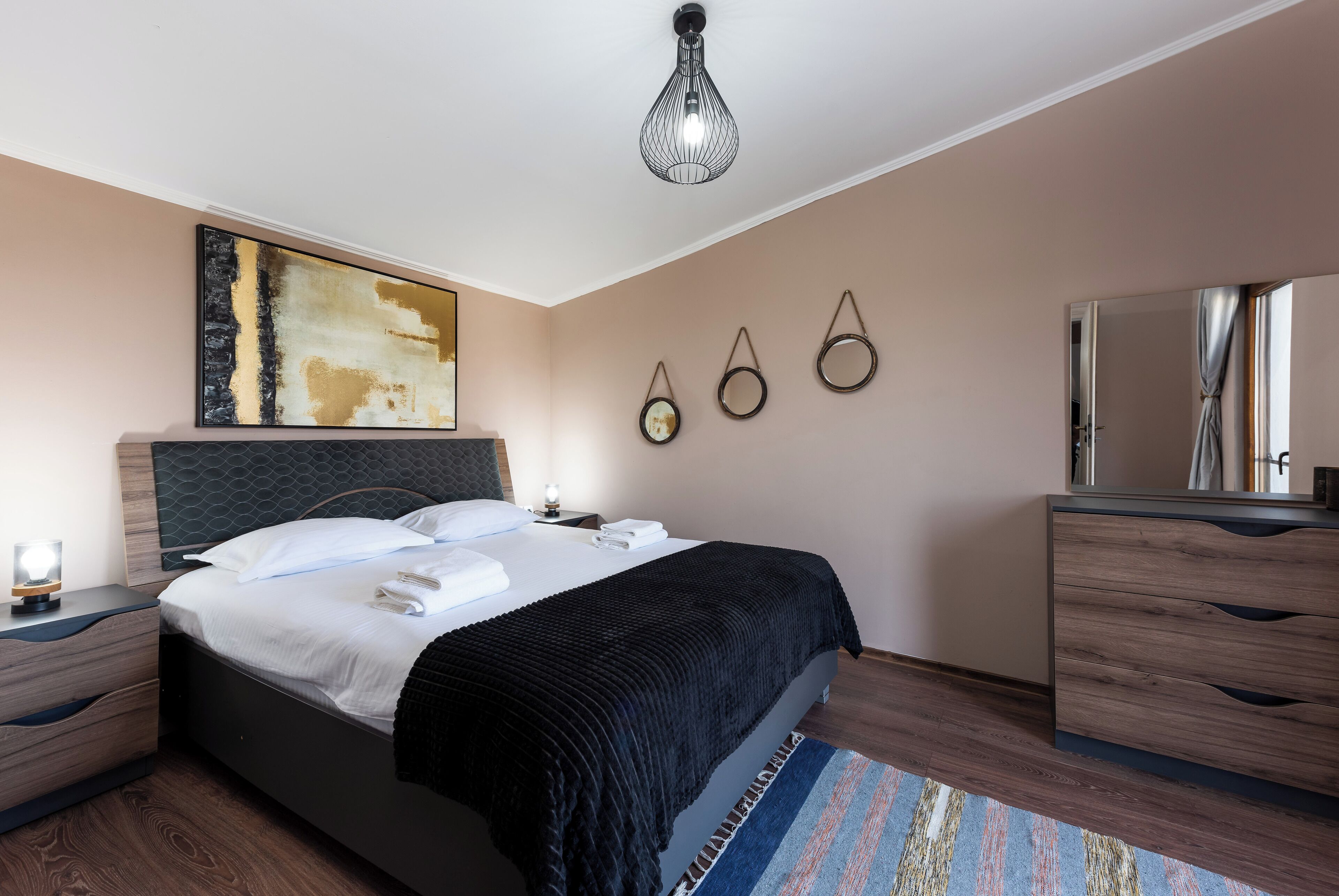 Una habitación de hotel moderna con una cama grande, una mesita de noche, un aparador, un espejo y una original pieza de arte en la pared.