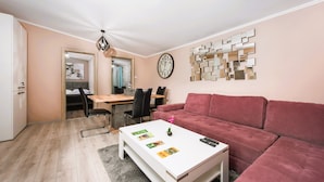 A living room with a white coffee table, a red sofa, a dining area with a wooden table and chairs, and a wall clock. - RAI Lodges (Zărnești)