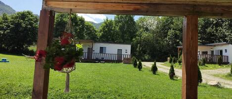 Une structure en bois formant une pergola, agrémentée d’une décoration suspendue, avec une pelouse verdoyante et, au fond, une caravane blanche.
