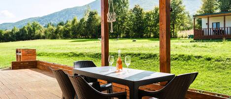 Un espacio de comedor al aire libre con mesa y sillas, con vistas a un campo cubierto de césped y montañas.