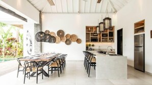 A modern kitchen with a central island, pendant lighting, and a dining area with a large table and chairs. - Canggu PETER 2 (Bali)