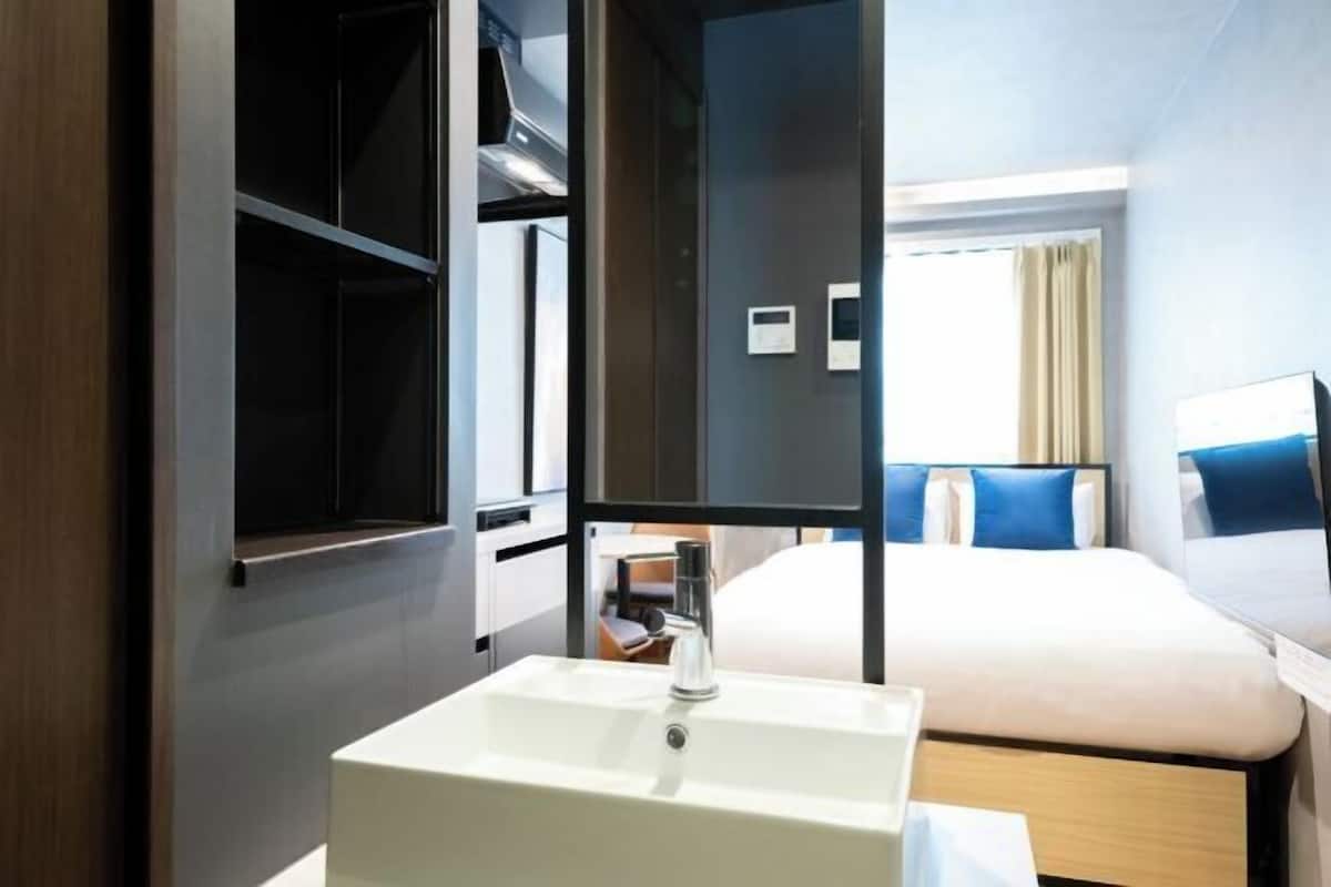 A hotel room with a white sink, a bed with blue pillows, and a view of the outside through a window.