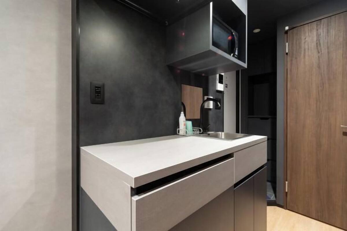 A modern kitchen with a white countertop, dark walls, and a wooden door.