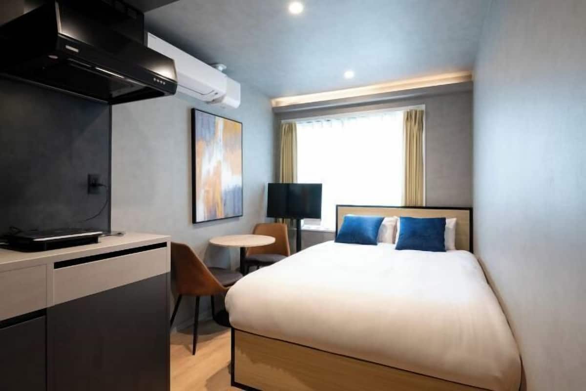 A hotel room with a bed, a desk, a chair, a small table, and a window with curtains.