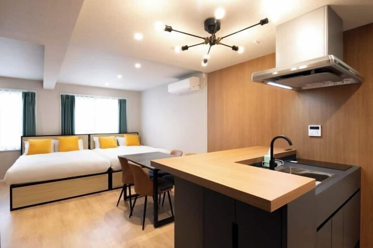A modern hotel room with a bed, a small kitchen area with a sink, and a dining table.