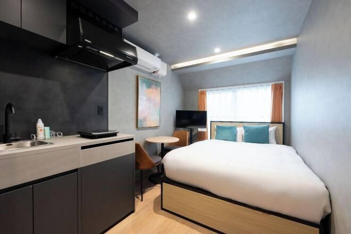 A compact hotel room with a kitchenette, a bed, a small table, and a TV.