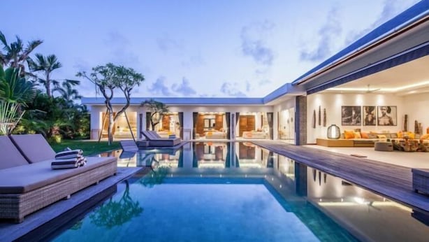 A modern house with a swimming pool, outdoor seating, and a well-lit interior.