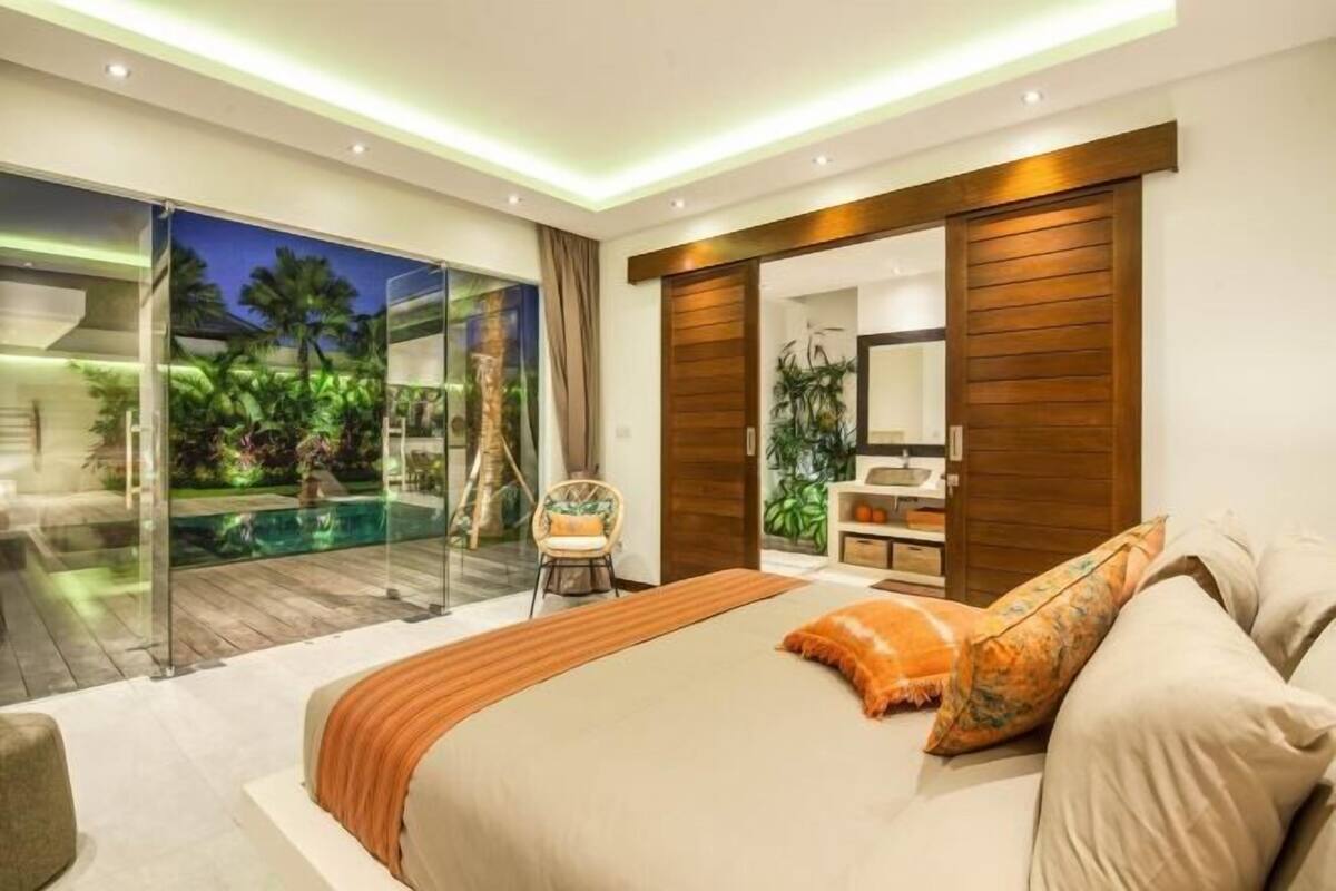 Ein modernes Schlafzimmer mit einem großen Bett, einer Glastür zum Pool und einer Holztür, die sich verschieben lässt.