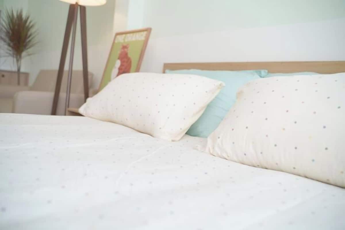 A neatly made bed with white and light blue pillows, a wooden headboard, and a framed picture on the wall.